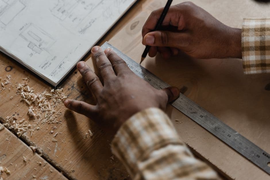 Hands of a craftsman measuring and drawing on wood in a workshop.
